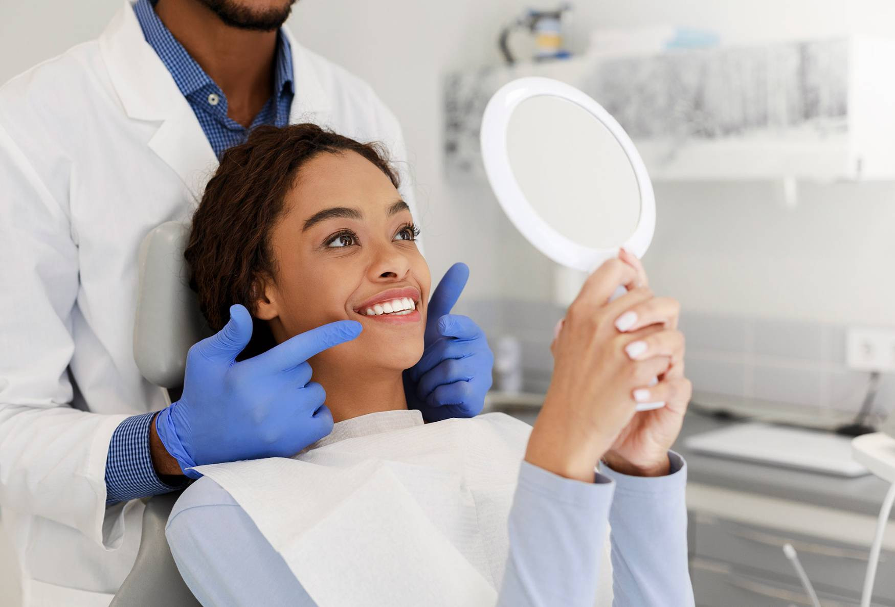 A smiling woman looking at her teeth in a dentist chair showing composite bonding results